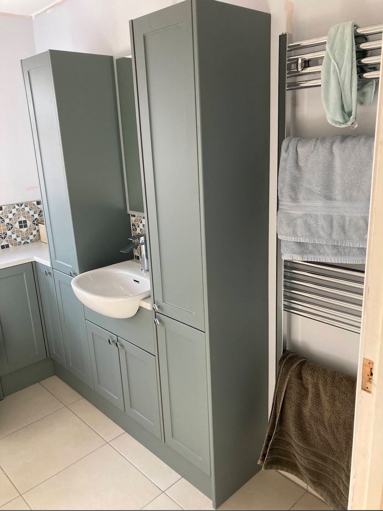 Sage-green fitted bathroom units with a basin, tall storage cabinets and a chrome towel radiator