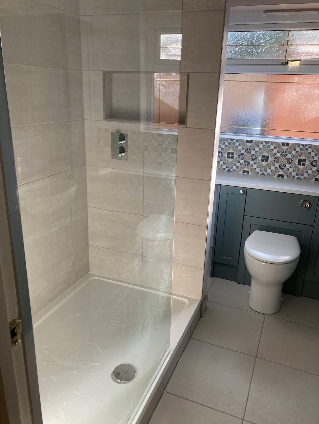 Walk-in shower with a glass screen and large pale tiles, and a sage-green fitted unit with a toilet beside it