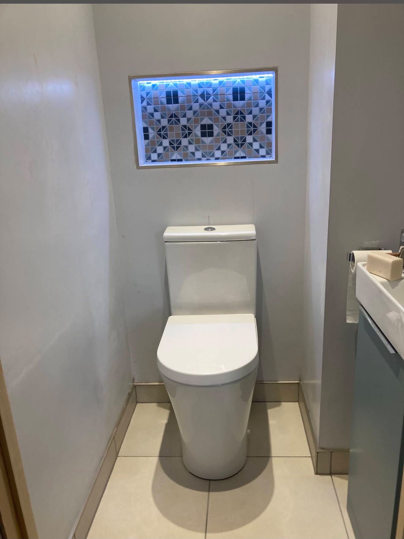 En-suite WC with a lit niche of blue, beige and white mosaic tiles above the toilet